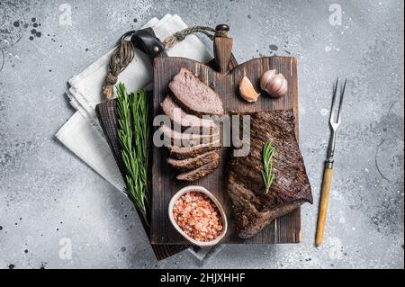 Roast and sliced tri tip beef steak on a wooden board with herbs. Gray background. Top view Stock Photo