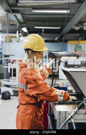 Young female industrial worker in uniform using manufacturing machinery at factory Stock Photo