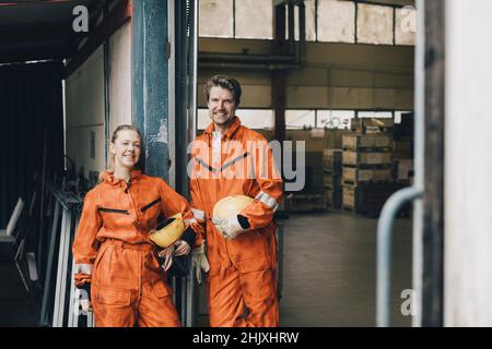 Portrait of confident male and female workers in uniform standing in warehouse doorway Stock Photo