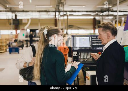 Senior businessman discussing with female manager over manufacturing machinery in factory Stock Photo