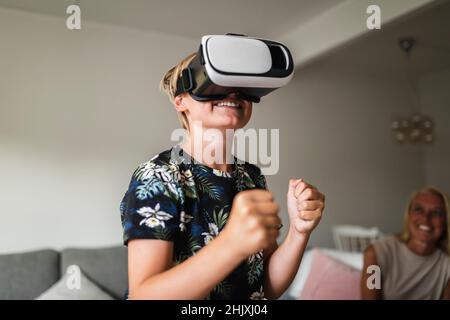 Smiling boy wearing virtual reality headset while mother sitting in background at home Stock Photo