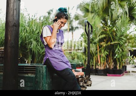 Happy female owner talking on smart phone in garden center Stock Photo