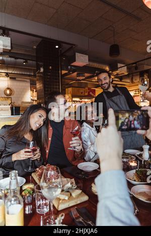 Cropped image of man taking picture of male and female friends through smart phone in restaurant Stock Photo