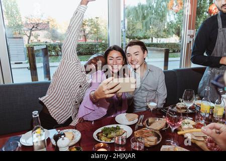 Woman taking selfie with male friends while celebrating in bar afterwork Stock Photo