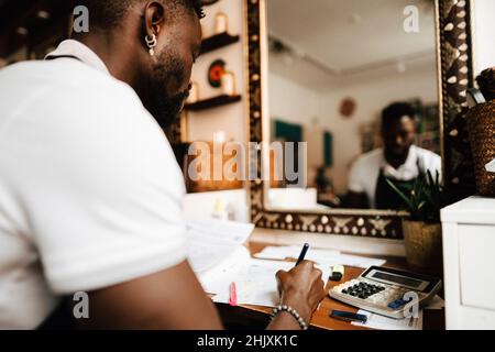 Male hairdresser calculating financial bill at table in barber shop Stock Photo