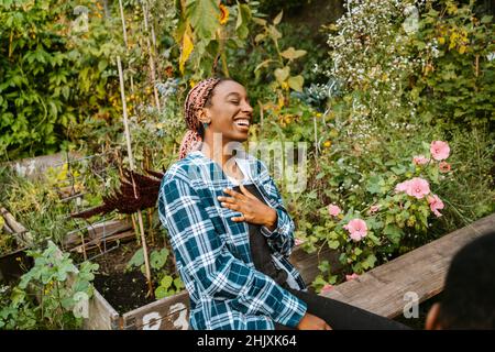 Cheerful young woman laughing while sitting in urban farm Stock Photo