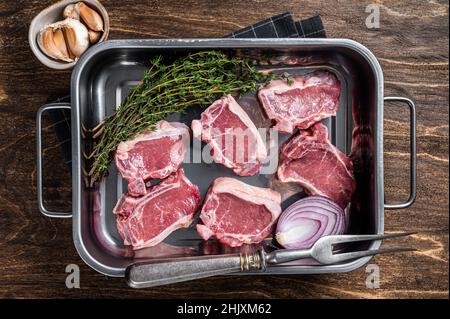 Uncooked Raw lamb loin chops steaks, saddle in kitchen tray with herbs. Wooden background. Top view Stock Photo