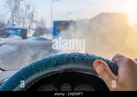 view of a man hand, the driver on the steering wheel inside the car, which is moving along a slippery, snow covered road behind a passenger bus Stock Photo