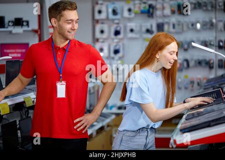 caucasian woman is looking for the best laptop in computer department of electronics store. Lady buyer chooses laptop in modern technology store, nice