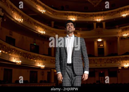 Showman. Young male entertainer, presenter or actor on stage. male public speaker speaking at microphone, performing presentation on stage, looking at Stock Photo