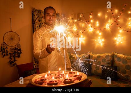 young man in traditional dress holding the fireworks in hand with ferry lights background image is taken on celebration of diwali. Stock Photo