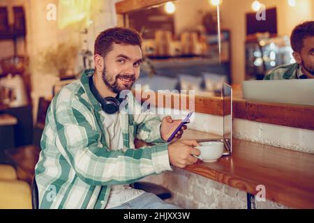 Joyful man using smartphone and laptop in cafe Stock Photo