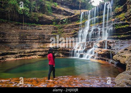 young girl standing near waterfall flowing streams falling from mountain at morning from low angle image is taken at wei sawdong falls cherrapunji soh Stock Photo