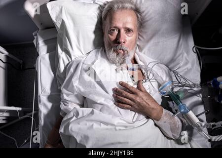 Sick Caucasian Man With Endotracheal Tube In Mouth Lying On Medical Couch, Bed In Hospital. Senior Elderly Ill Male Suffering From Coronavirus, Covid- Stock Photo