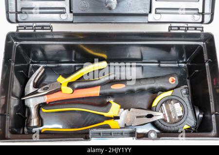 Black plastic box with the yellow and orange tools, which are: pliers, hammer and tape measure. Stock Photo