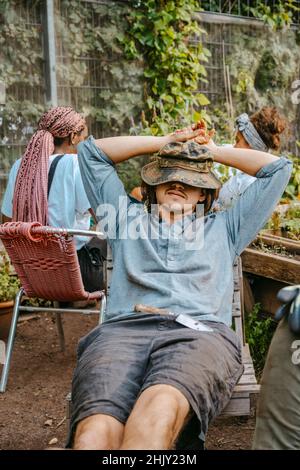 Young man with hands behind head resting in community garden Stock Photo