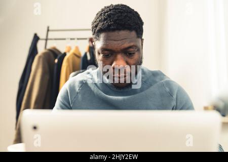 focussed intent black afroamerican working writing in front of white computer laptop tablet wearing light blue turtle neck long sleave - portrait shot. High quality photo Stock Photo