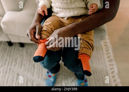 High angle view of father putting on sock to son in living room at home Stock Photo