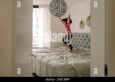 Cheerful girl jumping on bed in bedroom at home Stock Photo