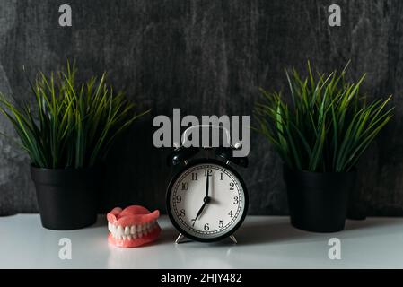 Full removable plastic prosthetic jaw and alarm clock. A denture next to the clock on the bedside table in the early morning. Dentures or false teeth Stock Photo