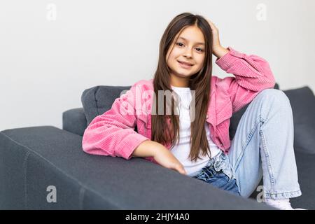 Photo of young cheerful lovely little girl happy positive smile hands touch chin dream dreamy sit couch home Stock Photo