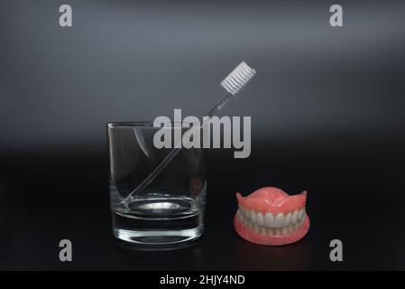 Full removable plastic denture of the jaws. Two acrylic dentures. Dental care with an toothbrush. Teeth and toothbrush on a dark background. Sound tee Stock Photo