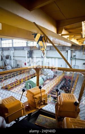 View from crane operator cabin. Yellow with black stripes overhead crane with hooks at petrochemical chemical plant. Inscriptions on boxes Stock Photo