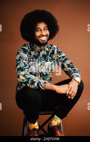 Portrait of smiling man sitting on stool against brown background Stock Photo