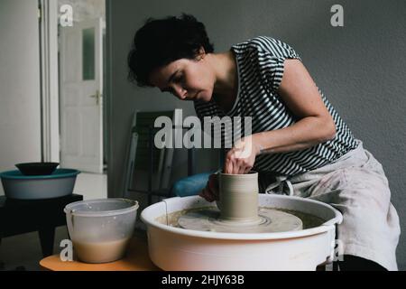Female potter modeling shape to pot at ceramics workshop Stock Photo