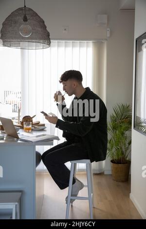 Young businessman drinking from glass while using smart phone at home Stock Photo
