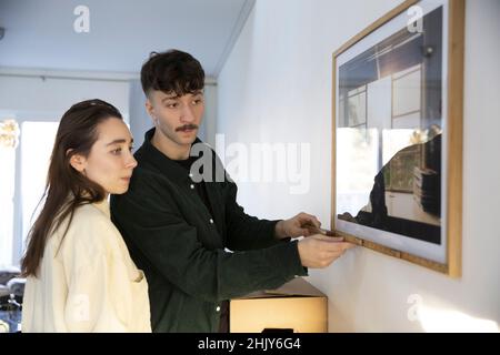Young man measuring picture frame standing by girlfriend at home Stock Photo