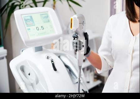 Close up of beautician hand in black glove holding ultrasound device for face lifting and skin tightening procedure. Young woman cosmetologist using modern cosmetology equipment in clinic. Stock Photo