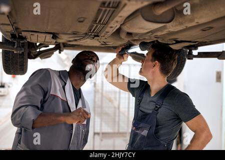 Team of diverse auto mechanics working on undercarriage of car diligence attention inspection examination annual checkup safety insurance professional Stock Photo