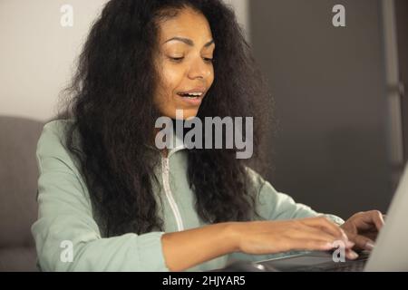 Young black business woman working on computer at home. Entrepreneur person typing text on laptop. Cheerful African female doing distant freelance wor Stock Photo