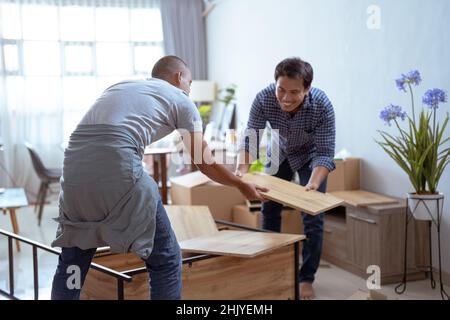 Two Male Movers Carrying a furniture and assmble it Stock Photo
