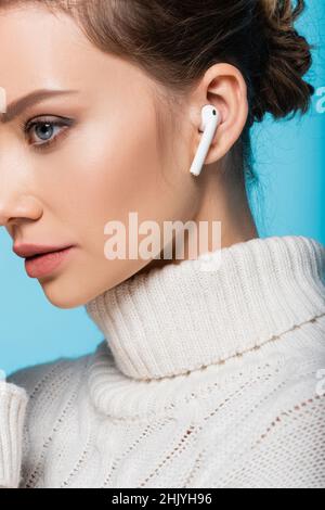 Cropped view of woman in knitted sweater and wireless earphone isolated on blue Stock Photo