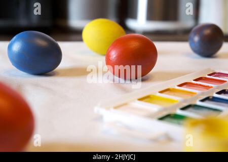 Colorful Easter eggs, paints, a nest on a white table in the dining room. Concept of preparation for Easter. Real authentic shot. Side View. Stock Photo