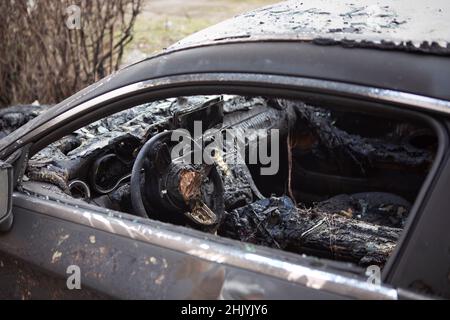 Burnt car interior close-up. Steering wheel and dashboard. Car after the fire. Car wreck burned by vandals or after explosion. Car accident on the roa Stock Photo