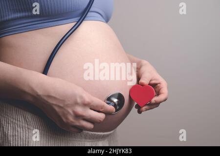 Pregnant woman listens to the baby heartbeat and movements with a stethoscope or fetoscope or Pinard Horn. Prenatal fetal health, anxiety, fear concept. High quality photo Stock Photo