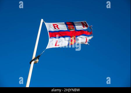 A worn RNLI flag blowing in the strong winds at the lifeboat station Cromer Norfolk Stock Photo