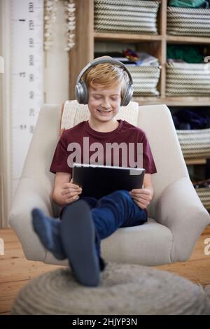 Boy Sitting In Chair In Bedroom At Home Wewaring Headphones And Playing On Digital Tablet Stock Photo