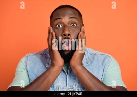 Photo of impressed pretty guy dressed jeans waistcoat big eyes arms cheeks isolated orange color background Stock Photo