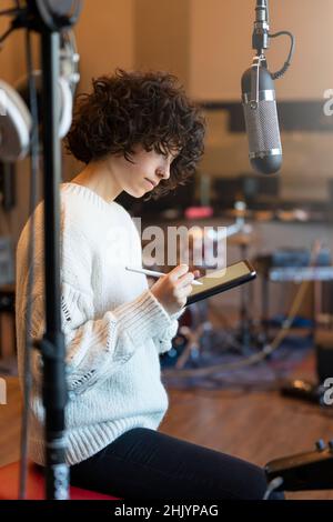 Young woman with curly hair sitting and thinking what to write in the music studio Stock Photo