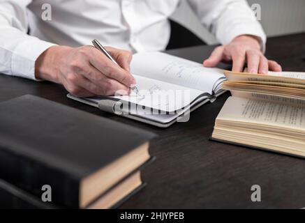Man hands taking notes in planner. Businessman sitting at table with books or codes at home or in office and writing thesis or thoughts. Learning and business education concept. High quality photo Stock Photo