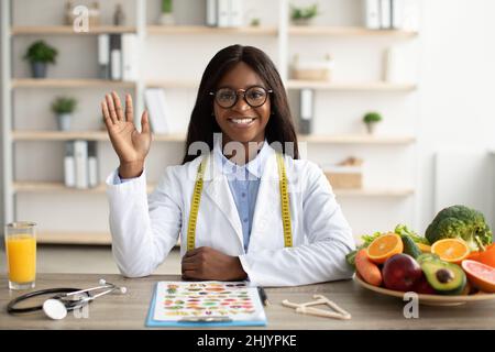 Portrait of happy african american nutritionist giving online consultations to patients, having video call in clinic Stock Photo