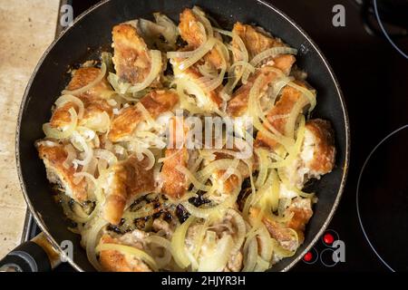 Delicious fried sea bass with golden onion rings in a frying pan. Top view. Home cooking of seafood Stock Photo