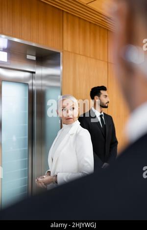 senior security man waiting for elevator near bi-racial bodyguard and african american security man on blurred foreground Stock Photo