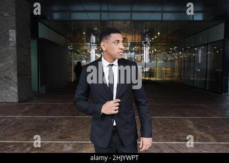 african american security man in formal wear looking away near entrance of hotel outdoors Stock Photo