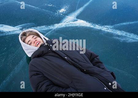 Teenager lies on his back on the frozen ice of Lake Baikal. Stock Photo