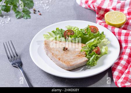 Grilled tuna steak with salad on white dish on concrete table. Stock Photo
